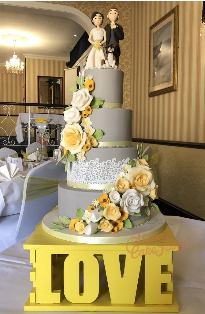 four tier grey wedding cake with yellow sugar flowers, cake lace and bride and groom cake topper